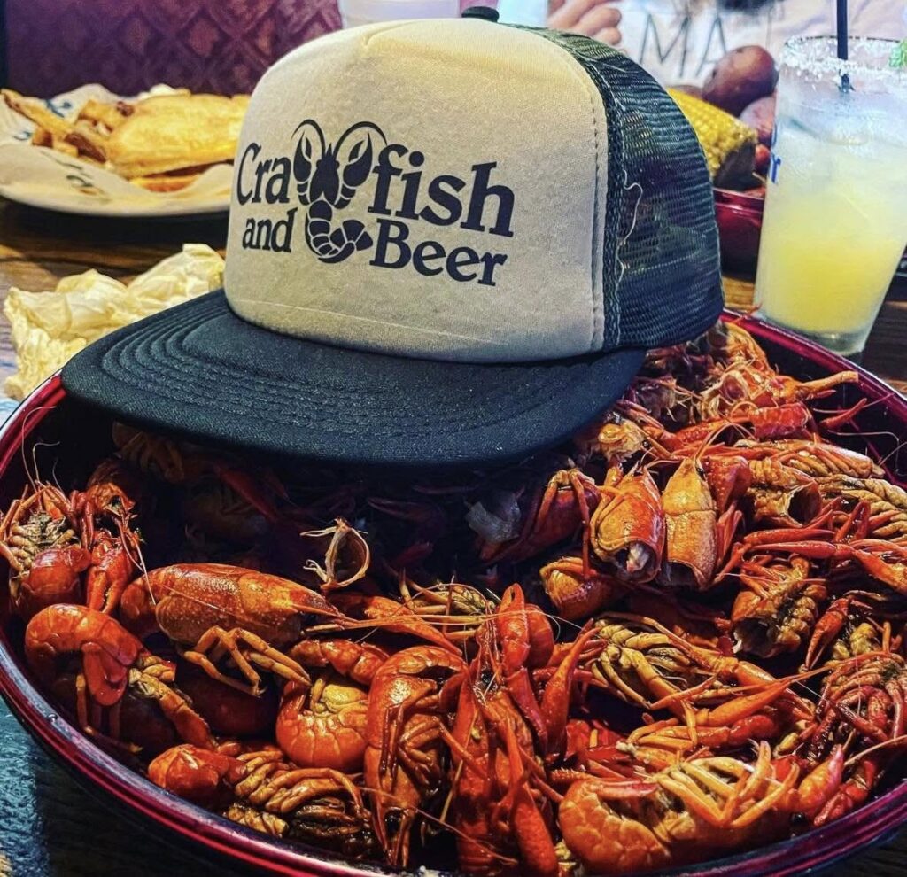 Crawfish and Beer trucker hat over a tray of boiled crawfish